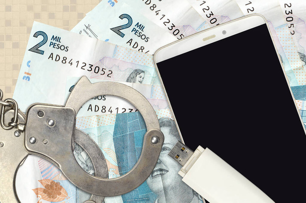 2 Colombian pesos bills and smartphone with police handcuffs. Concept of hackers phishing attacks, illegal scam or online spyware soft distribution - Photo, Image