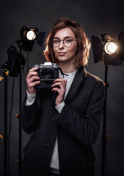 Schöne rothaarige Fotografin hält eine Digitalkamera in der Hand und schaut auf die Kamera - Foto, Bild