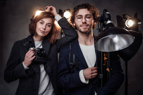 Zespół dwóch fotografów posiada aparat cyfrowy i sprzęt oświetleniowy pozowanie w studio - Zdjęcie, obraz