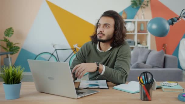 Thoughtful Arab entrepreneur using laptop typing then thinking working at desk alone - Кадри, відео