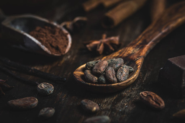 Gros plan de cuillère en bois avec des fèves de cacao et une cuillère en bois avec de la poudre de cacao, décorée avec des épices de cuisson. - Photo, image