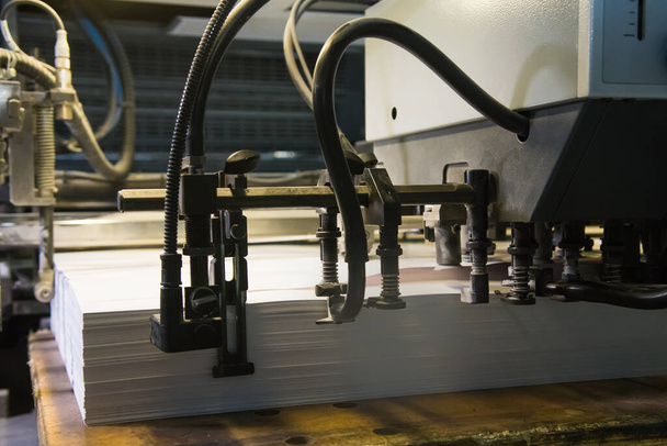 Drukpersen aan het werk bij het drukken. Bedrukte vellen papier worden geserveerd in de drukpers - Foto, afbeelding