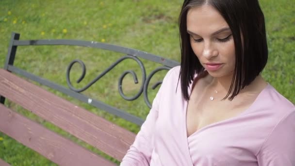 Elegante joven morena relajándose en el banco en el parque
 - Metraje, vídeo