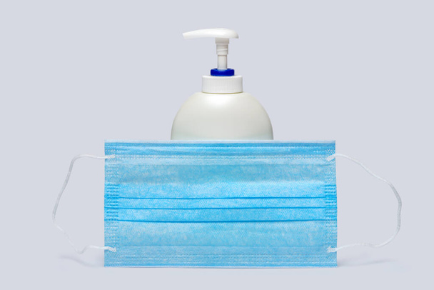 bottle of lotion, sanitizer or liquid soap and protective mask over light grey background - Фото, зображення