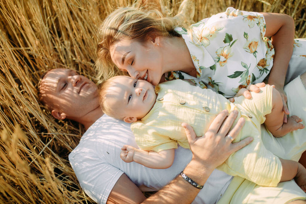 Szczęśliwa młoda rodzina z dzieckiem leżącym i odpoczywającym wśród żółtego pola pszenicy. Zbliżenie. - Zdjęcie, obraz
