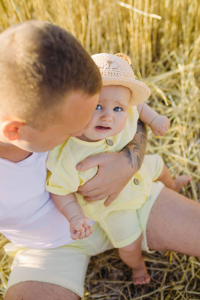 Happy father sits and plays with his baby among yellow wheat field. - Photo, Image