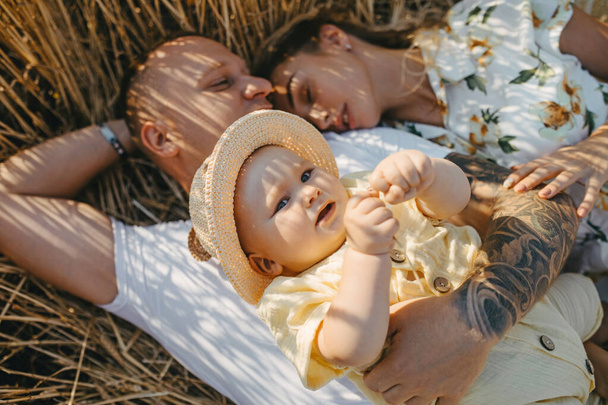 Onnellinen nuori perhe, jossa vauva makaa ja lepää keltaisen vehnäpellon keskellä. lähikuva-analyysi. - Valokuva, kuva