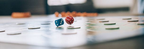Επιτραπέζιο παιχνίδι και τα χέρια ζαριά ρολό γκρο πλαν. Κύβοι παιχνίδι πετούν πάνω από ένα ξύλινο τραπέζι και με φόντο ένα πολύχρωμο, φωτεινό παιχνίδι του σκάφους - Φωτογραφία, εικόνα
