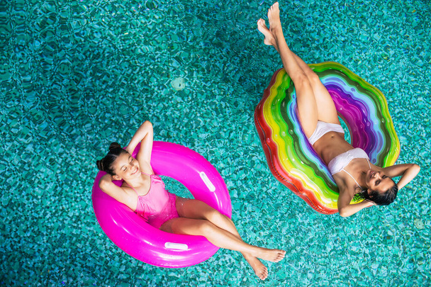Foto vista superior completa desfrutando de bronzeado do sol, mãe feliz e filha em biquínis nos colchões infláveis na piscina. Férias de Verão. Relaxar na piscina do hotel. Descanso familiar
 - Foto, Imagem