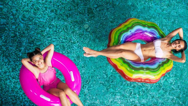 Full-length top view photo enjoying of suntan, happy mother, and daughter in bikinis on the inflatable mattresses in the swimming pool. Summer Vacation. Relaxing in the Hotel pool. Family rest - Fotoğraf, Görsel