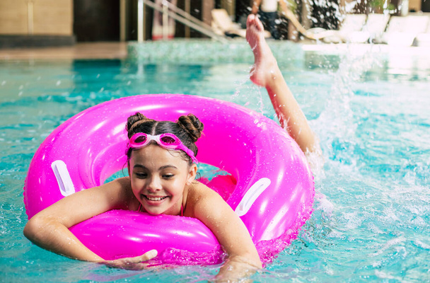 Happy little girl in goggles playing with a pink inflatable ring in the swimming pool on a hot summer day. Kids learn to swim. Child water toys.Family beach vacation. - Foto, afbeelding
