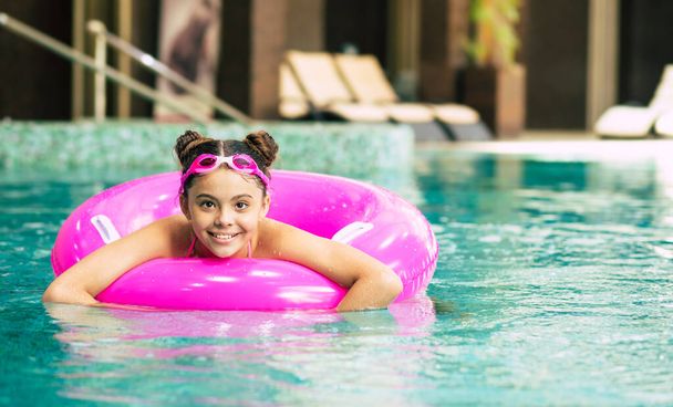 Happy little girl in goggles playing with a pink inflatable ring in the swimming pool on a hot summer day. Kids learn to swim. Child water toys.Family beach vacation. - Foto, imagen