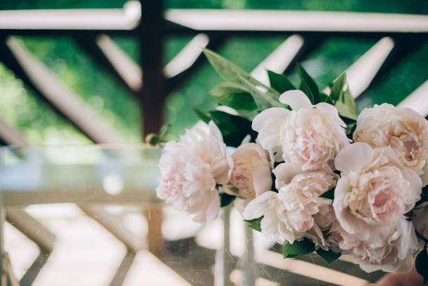 Stillleben eines frischen Straußes geschnittener rosa Pfingstrosen. Ein Strauß Pfingstrosen liegt auf einem Glastisch auf der Veranda vor dem Hintergrund eines grünen Gartens an einem hellen Tag. - Foto, Bild