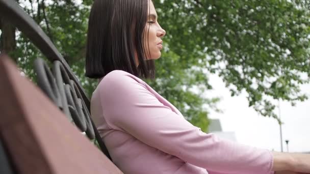 Elegante jonge brunette ontspannen op bank in park - Video