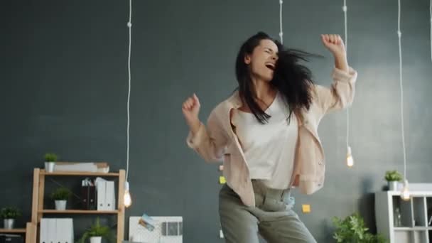 Slow motion of joyful young woman dancing on office desk and enjoying music - Filmagem, Vídeo