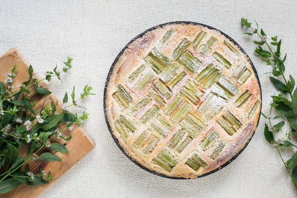 Ciasto rabarbarowe na patelni na lekkim rustykalnym materiale włókienniczym z miętową zielenią w tle - Zdjęcie, obraz