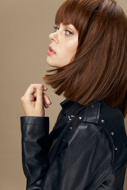 Young beautiful woman posing on a beige background in the studio in a black leather jacket - Photo, image