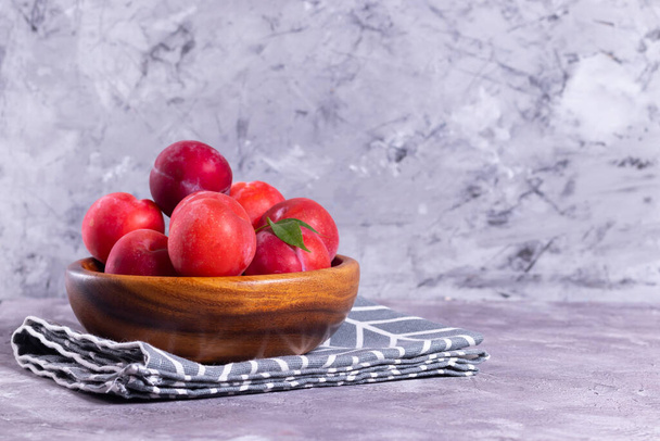 Ripe plums in a wooden plate with a tissue napkin on a gray background - Valokuva, kuva