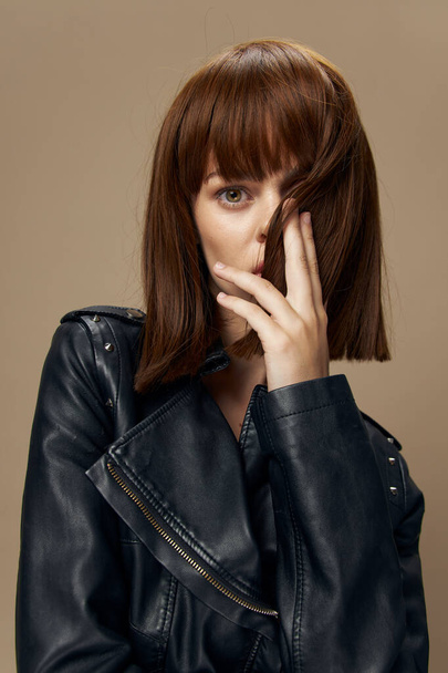 Young beautiful woman posing on a beige background in the studio in a black leather jacket - Photo, Image