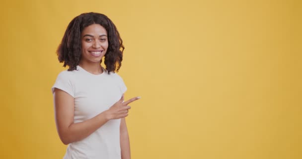 Χαρούμενη μαύρη κοπέλα που δείχνει στην άκρη το χώρο των αντιγράφων και χαμογελά - Πλάνα, βίντεο