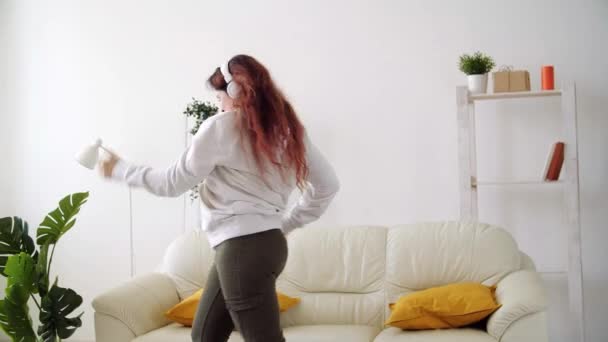 Happy woman listening to music and dancing in living room - Materiaali, video