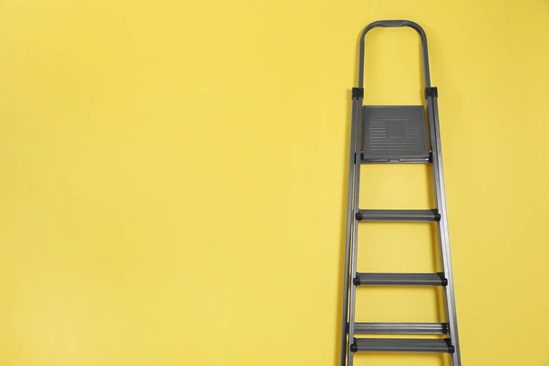 Metal stepladder on yellow background. Space for text - 写真・画像