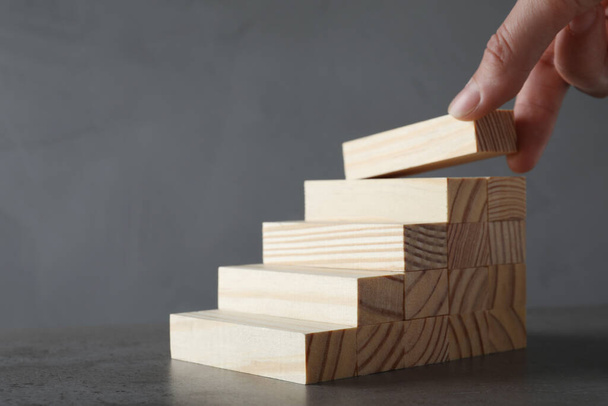 Woman building steps with wooden blocks on grey table, closeup. Career ladder - 写真・画像