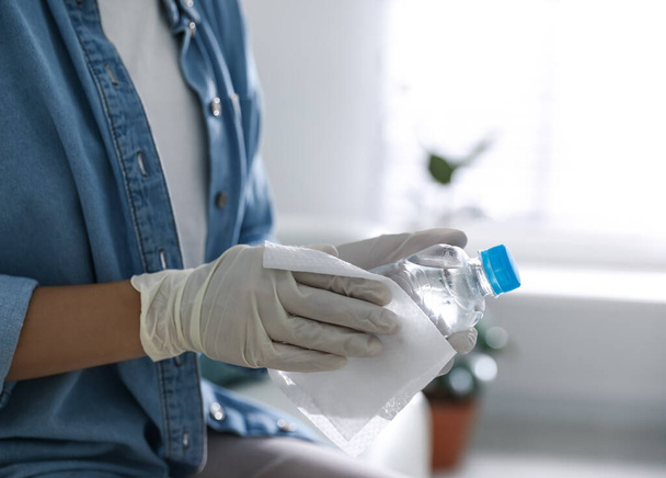 Woman cleaning bottle of water with wet wipe indoors, closeup - Φωτογραφία, εικόνα