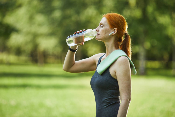 Spor salonundaki kadın parkta su içiyor. - Fotoğraf, Görsel