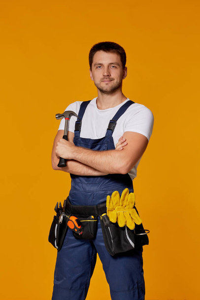repairman worker in yellow hard hat and uniform holding hammer. - Фото, изображение