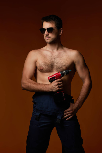 sexy biały mężczyzna pracownik w kombinezony trzymając bezprzewodowy śrubokręt - Zdjęcie, obraz