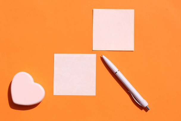 Colored sheets of paper for notes and a small heart on an orange background. Close-up. Top view, copy space. - Photo, Image