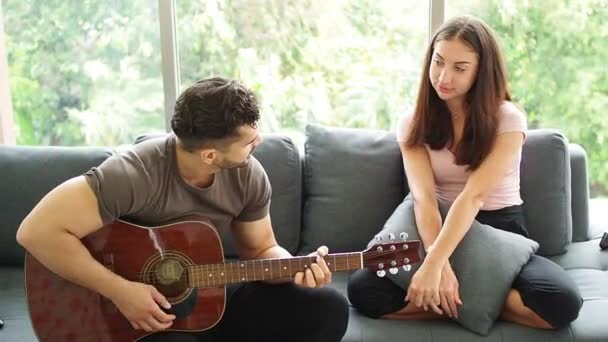 Male PLaying guitarwith his wife girlfriend at home in living room. Man playing love songs for lover. concept celebrating, Happy couple playing a guitar and singing a song together at living room. - Footage, Video
