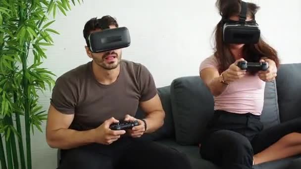 Pariskunnalla VR tai virtuaalitodellisuus lasit, kuulokkeet istuu ja pelaa videopeli sohvalla kotona teknologian ja innovoinnin konsepti. Pidän hauskaa. Viihdekäsite. - Materiaali, video