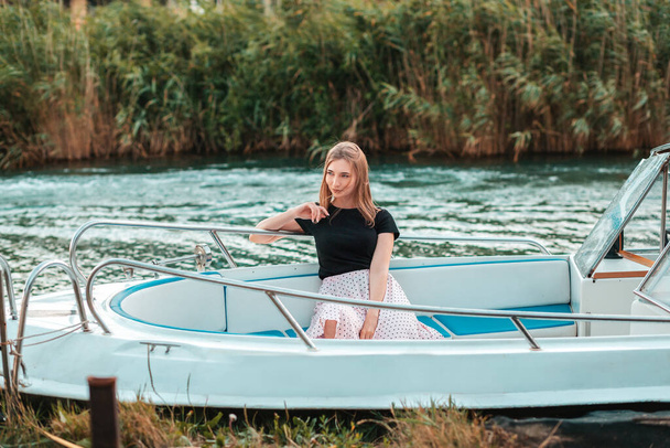 Nyári szünet. Egy elegáns nő ül egy kék csónakban, lebeg a folyón. Reeds a háttérben. Fénymásolási hely. - Fotó, kép