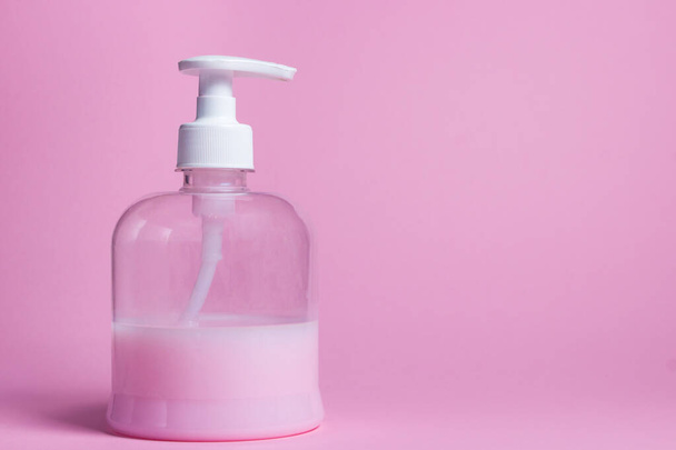 Roze zeep op een roze achtergrond. De fles zit half vol met vloeibare zeep. Handhygiëne - Foto, afbeelding
