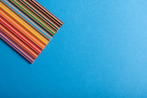 Composition en diagonale de crayons de couleur arc-en-ciel sur fond bleu représentant la diversité à l'école - Photo, image