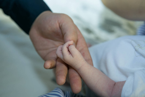 Kinder. Babys. Kinderbetreuung. Kleine Hand eines Neugeborenen in der Hand eines glücklichen Elternteils - Foto, Bild