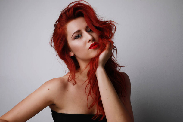 Headshot of attractive young woman with long red hair, and bright make-up, posing over grey background. - Foto, imagen