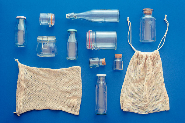Yläpuolella näkymä lasipurkit ja pullot sinisellä pohjalla. Eco pussit käytetään ostoksia ostoksia. Ei-muoviset astiat kotitalouskäyttöön keittiö ja ostokset. - Valokuva, kuva