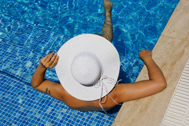 mujer joven en un sombrero blanco relajándose en la piscina - Foto, Imagen