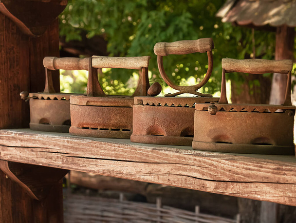 antik faszén vasalók. Vintage vasalók sorban fa polcon.Régi vágású vasalóeszközök.Örökség koncepció - Fotó, kép