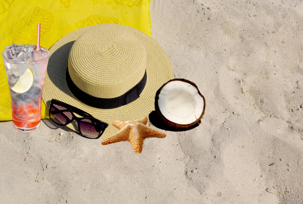 Chapeau, lunettes de soleil, noix de coco et étoiles de mer sur le sable - Photo, image