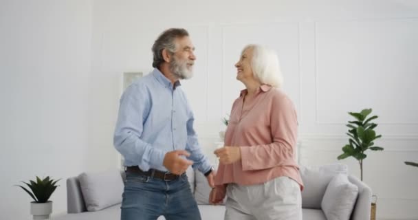 Caucasian old gray-haired married couple dancing at home and smiling. Senior beautiful woman and handsome man looking at each other with love and dance. Male and female pensioners listening to music. - Footage, Video
