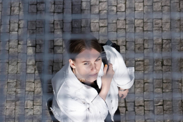 Een jonge vrouwelijke toerist in een wit jasje en met een rugzak.Uitzicht van boven door het raster.Kijkend naar de zijde.Geometrische lijnen.Het glurende effect.stedelijke achtergrond.casual stijl.lifestyle - Foto, afbeelding