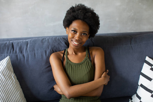 Happy african American young woman looking in camera sit relax on cozy couch happy to move to new apartment. Smiling black girl rest on comfortable sofa in living room dreaming - Fotografie, Obrázek