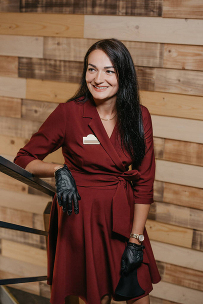 Eine lachende Restaurantmanagerin in schwarzen Einweghandschuhen, die in einem Café posiert. Eine freundliche Café-Besitzerin in einem rubinroten Kleid wartet auf Kunden. - Foto, Bild