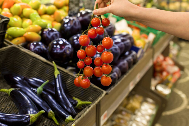 Kobieca ręka wybiera świeże pomidory w supermarkecie. Pojęcie zdrowej żywności, bio, wegetariańskie, dieta. - Zdjęcie, obraz