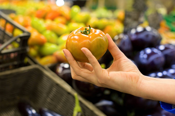 スーパーで新鮮なトマトを選ぶ女性の手。健康食品、バイオ、ベジタリアン、食事の概念. - 写真・画像