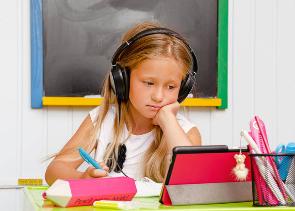 Causacian mignon écolier avec écouteurs est sur ennuyeux éducation à la maison en ligne. Concept d'enseignement à distance. - Photo, image